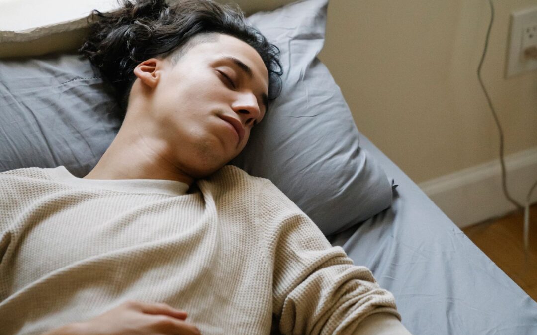 Jonge man slaapt in bed met zijn smartwatch en telefoon naast zich, zijn hartslag zakt in de nacht